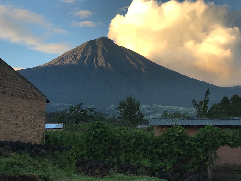 View of Mount Sabinyo with lush green surroundings at Volcanoes National Park, Rwanda, under a partly cloudy sky.